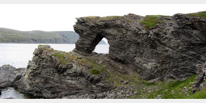 Das wohl am meisten fotografierte Motiv des Felsentores Kirkeporten.  Im Hintergrund sind die 300 Meter hohen Felsen zu sehen, auf dem sich das Nordkap befindet. Genau im Tor das markante Nordkapp-Hornet unterhalb des Kaps.
