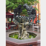 Eltville - Marktplatzbrunnen, der Marktplatzbrunnen symbolisiert mit vielen Einzelheiten die Eltviller Geschichte. Hauptmotiv ist ein mit Weinfssern beladener Kahn, der von Rosenstrauch und Weinstock als Symbol des wirtschaftlichen Reichtums umrankt wird