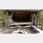Im Hiidenportti-Nationalpark  Porttilampi, eine typische Schutzhtte in finnischer Wildnis: Feuerstelle, Feuerholz, ein Eisengrill und Eisenspiee zum Halten des Fleisches. Selbst der Wassereimer ist da, um nach der Party alles wieder in Ordnung zu bring