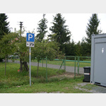Das Bild zeigt den Mast vom Parkplatzschild mit dem WoMo-Aufkleber, daneben eine ffentliche Toilette